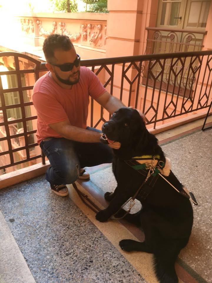 Foto do Francis, que está agachado e passando as mãos no cão-guia Elmo