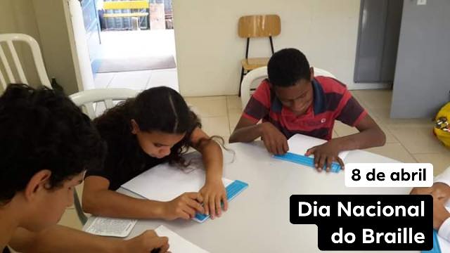 Foto mostra três crianças atendidas pela ADEVIC lendo Braille.São dois meninos e uma menina ao centro, e estão sentados em torno de uma mesa redonda e branca, no ambiente de uma sala de aula da entidade. No rodapé da imagem, o texto: 8 de abril: Dia Nacional do Braille.