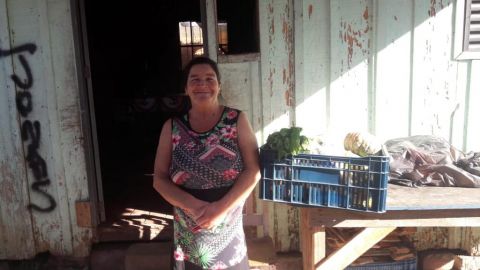 Mulher em frente a residência sorri ao lado da caixa de alimentos.