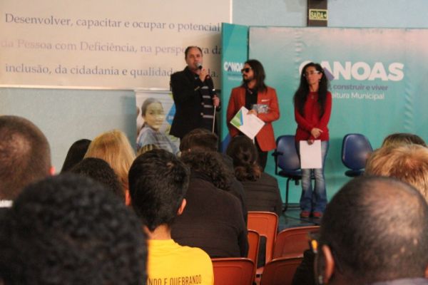 Em um palco, o vice-presidente da ADEVIC, Eri, fala para os participantes do evento