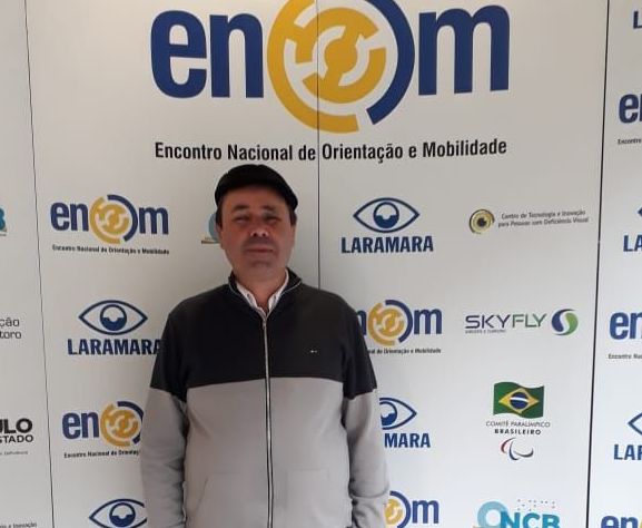 Vice-presidente Eri Domingos da Silva posa para foto em frente a um banner do ENOM