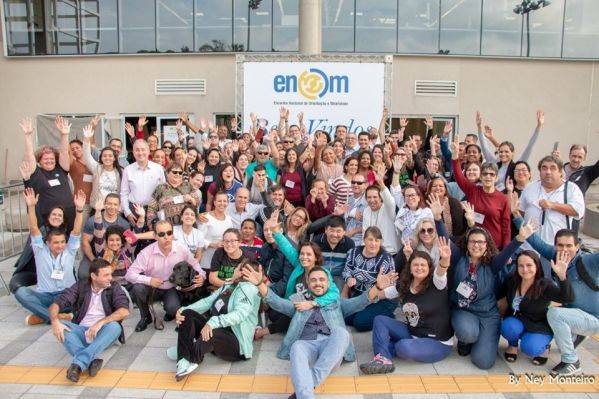 Participantes do encontro posam para foto coletiva. O grande grupo está na área externa do evento