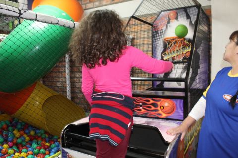 Menina associada da ADEVIC brinca em uma mini tabela de basquete. Ela acaba de jogar a bola verde na cesta e a bola está equilibrada no aro da tabela