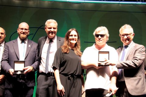 No palco do evento, o prefeito entrega a medalha ao presidente da Adevic, José Guimarães. Ao lado dele estão também a vice-prefeita e diversas outras pessoas. 