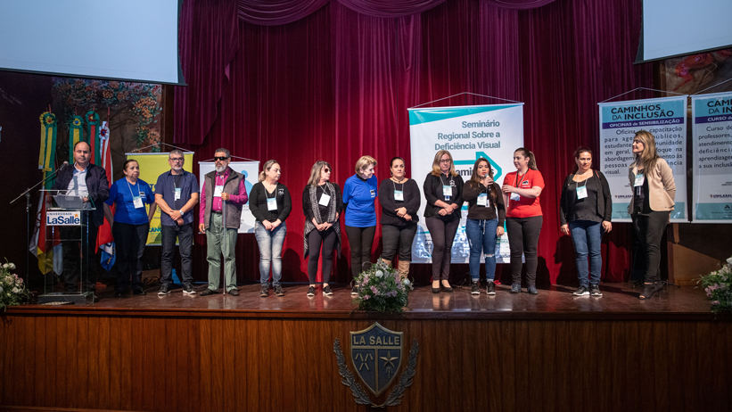 Equipe da ADEVIC no palco do salão de atos da Unilasalle durante a cerimônia de abertura do Seminário