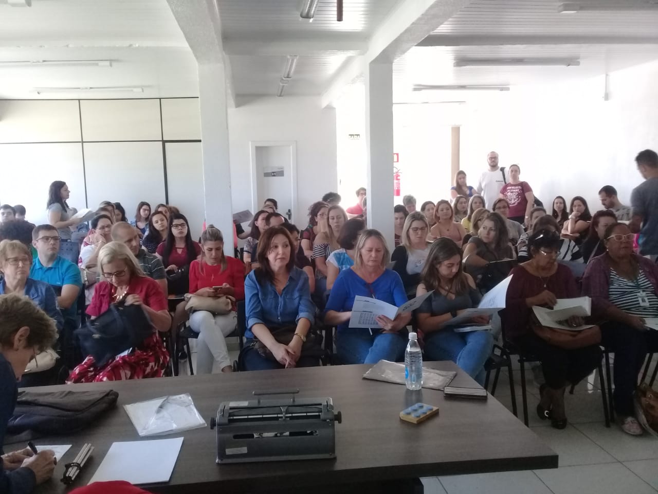 Um grande grupo de pessoas sentadas formam uma plateia no local de realização do workshop